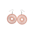 Pair of pink round wooden earrings with open circular centres, radiating sunburst cut-outs and silver-tone hook ear wires on a white background
