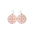 Pair of pink round wooden earrings with symmetrical floral openwork and curling decorative cut-outs, with silver-tone hook ear wires on white