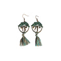 Pair of bronze-tone tree of life earrings with green accents, small dangling details and green and brown tassels on a white background